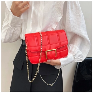 Detail of red quilted crossbody bag with gold chain strap and buckle on white shirt