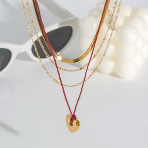 Detail of layered gold snake chains, bead necklace, and red heart pendant necklace