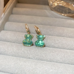 Vue macro de boucles d'oreilles ours dorées avec breloques en résine vert menthe et zircon
