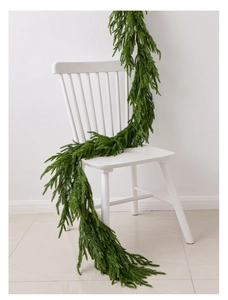 Close-up of natural green Norfolk pine garland draped over a white wooden chair