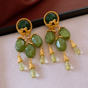 Macro detail of vintage gold fringe earrings with emerald green gemstone resin pendants