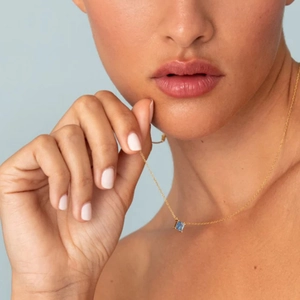 Macro detail of square blue zircon pendant on a gold chain worn on the neck
