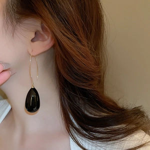Détail d'une boucle d'oreille crochet dorée avec un grand pendentif goutte noir porté