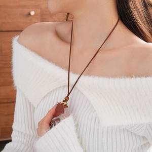 Detail of red-brown geometric pendant on leather cord necklace worn over a white sweater