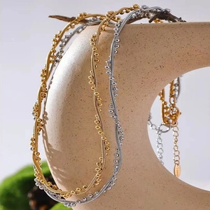 Gold and silver stainless steel snake chain necklace with beads on a beige display