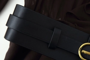 Detail of a black leather belt with a round gold metal buckle on a dark dress