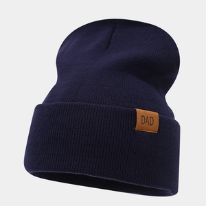Detail of navy blue ribbed knit beanie featuring a premium brown leather DAD patch logo