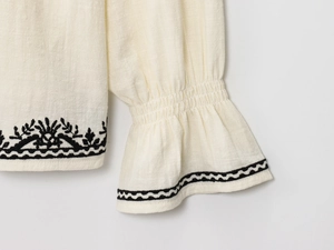 Détail de la broderie ethnique noire sur les manches d'une blouse en lin crème