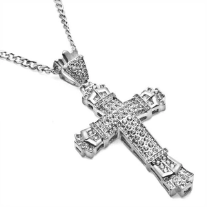 Détail d'un collier pendentif croix évidée en argent avec pierres étincelantes et maille.