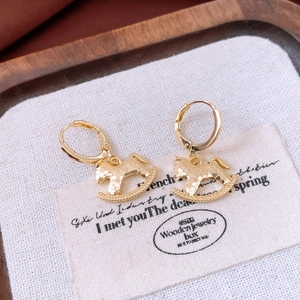 Détail de boucles d'oreilles cheval à bascule plaquées or 18 carats sur lin blanc
