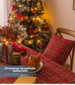 Detail of red and green plaid Christmas tablecloth with white snowflake patterns and festive decor