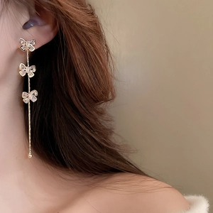 Detail of long linear bow earrings with zircons and gold tassels worn by a model