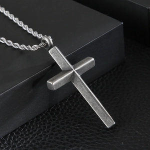 Close-up of vintage silver cross pendant with twisted rope chain on dark leather