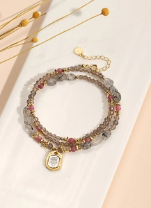 Detailed shot of multi-layer beaded bracelet with grey rutilated quartz and gold face charm