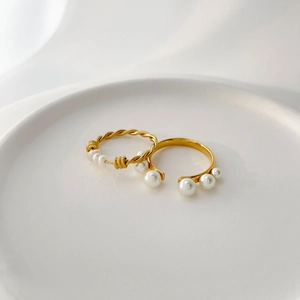 Minimalist gold-plated twist rings with white pearl accents on white tray