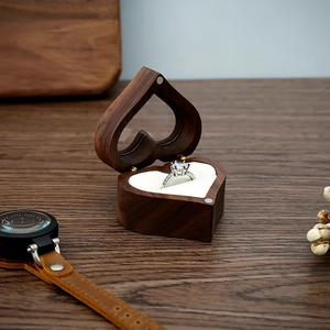 Handcrafted heart-shaped wooden ring box with silver solitaire ring on wooden background