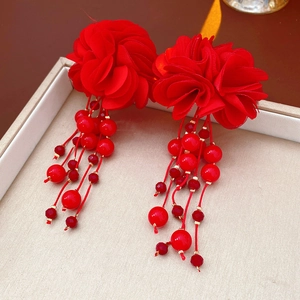 Vue détaillée de boucles d'oreilles fleurs en tissu rouge avec glands perlés sur écrin
