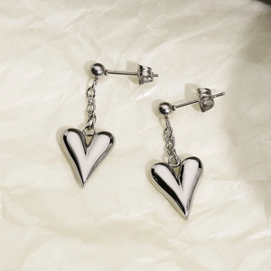 Close-up of silver titanium steel heart earrings with 3D pendant on beige paper
