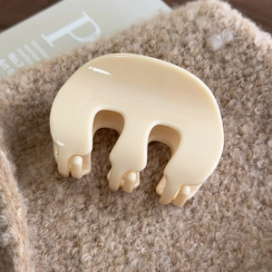 Close-up of cream acrylic M-shaped hair claw clip on soft textured fabric backdrop