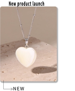 Detailopname van hartvormige schelphanger aan zilveren kralenketting op steen