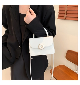 Detailed shot of a white PU leather crossbody bag with a round gold buckle closure