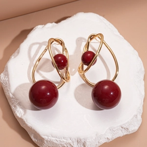 Close-up of geometric earrings with gold wire and red beads on a white marble slab