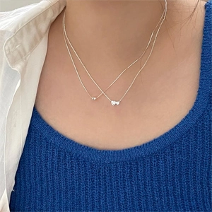 Detail of layered sterling silver necklaces with heart zircon pendants on a model