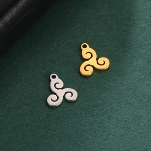 Polished gold and silver stainless steel Triskele pendants on a dark textured background