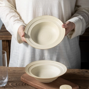 Artisanal beige stoneware pasta bowl with spiral texture in a warm lifestyle setting
