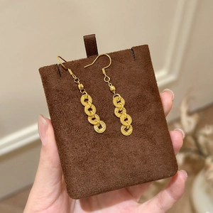 Close-up of gold Chinese coin tassel earrings with textured rings on brown suede