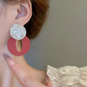 Close-up of geometric acrylic earrings with white marble stud and red matte ring detail