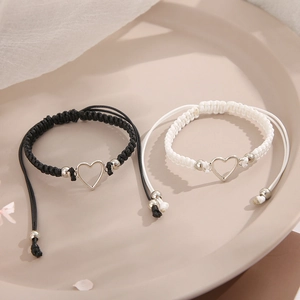 Adjustable woven friendship bracelets with silver hollow heart charms on a beige tray
