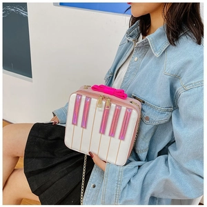 Creative piano-style crossbody bag with pink bow and gold chain on model for size reference