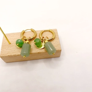 Macro shot of gold hoop earrings with green gemstone beads and cylindrical jade charms