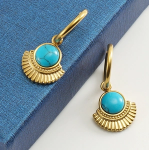 Close-up of gold fan-shaped earrings with turquoise stones on a blue textured box
