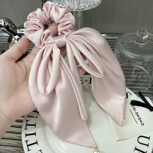 Elegant pink satin bow hair scrunchie with pearl ends shown in a soft aesthetic setting