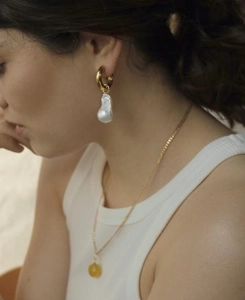 Baroque pearl drop earrings and gold necklace set worn by a model in a warm setting