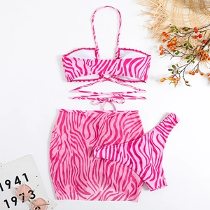 Flat lay of pink zebra print 3-piece bikini set with matching mini skirt and sun accessories