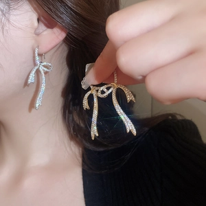 Detailed view of silver bow earrings with sparkling cubic zirconia on model and held in hand