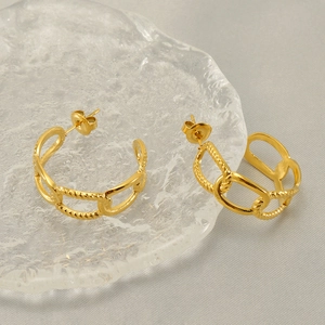 Boucles d'oreilles créoles dorées en acier titane sur un support en verre texturé
