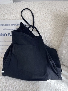 Minimalist large black canvas tote bag with front pocket on a white textured background
