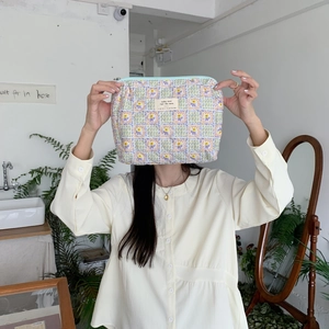 Floral makeup pouch with pastel patterns and blue zipper held in a cozy home setting
