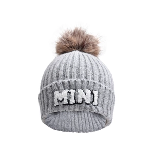 Detail of grey knitted beanie with MINI embroidery and brown faux fur pom-pom topper