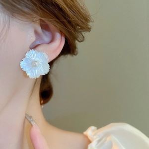 Elegant white shell flower stud earrings with a pearl center on a female model