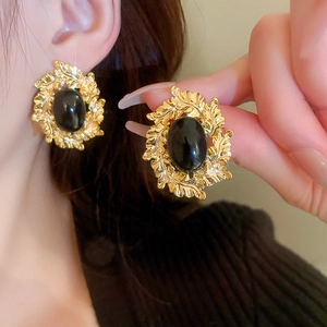 Detaillierte Nahaufnahme goldener Blattohrringe mit schwarzen ovalen Edelsteinen am Model