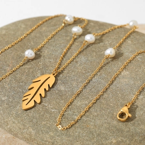 Golden hollow feather pendant necklace with white natural pearls on a gray textured rock