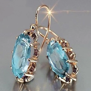 Detalle macro de pendientes de gancho dorados con circón azul claro y engaste ondulado