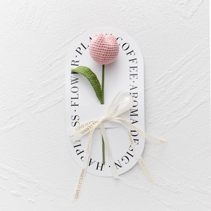 Close-up of pink handmade crochet tulip on white gift card with decorative ribbon