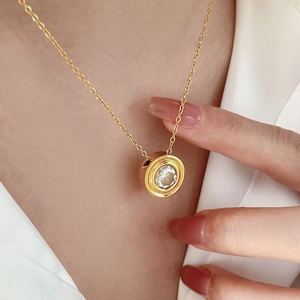 Close-up of golden necklace with a round zircon pendant worn by a model