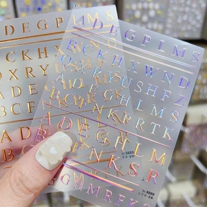 Dettaglio macro di adesivi per unghie 3D a rilievo con lettere dorate e olografiche
